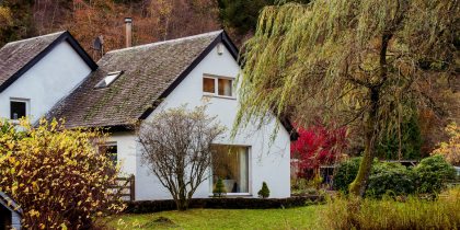 White brick house next to scenic woodland and lake