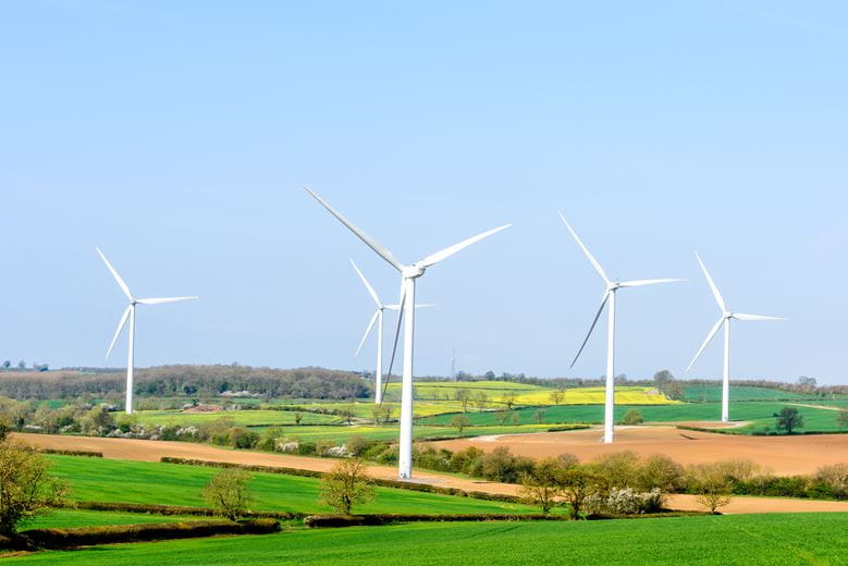 landscape of fields with four wind turbines against a sunny sky